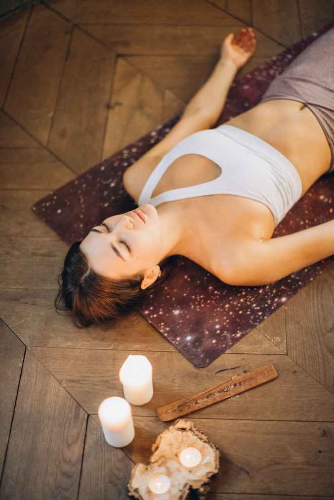 Woman laying on yoga mat with eyes shut and candles around her