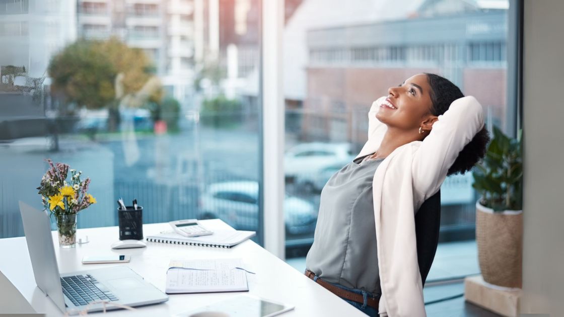Woman in a window office smiling and leaning back in her chair.
